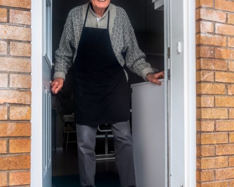 man in black vest and black dress pants standing beside white wooden door