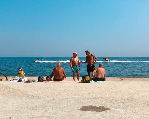 3 women and 2 men sitting on beach sand during daytime