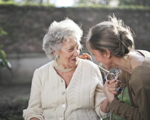 Joyful interaction between an elderly woman and her granddaughter in a sunny outdoor setting.