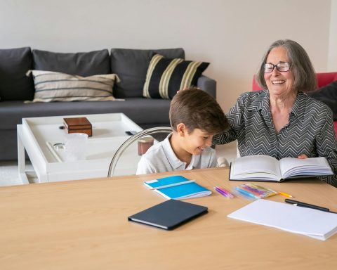 Happy grandmother assisting her grandson with homework indoors, creating a joyful learning atmosphere.