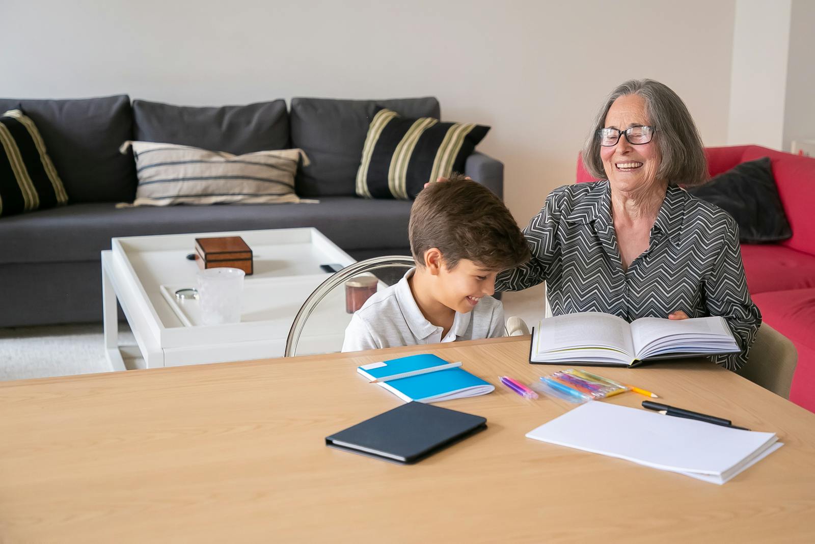 Happy grandmother assisting her grandson with homework indoors, creating a joyful learning atmosphere.