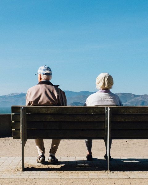 man and woman sitting on bench facing sea