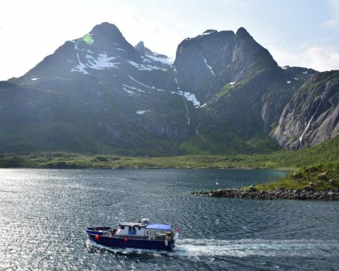 white and blue boat on water near mountain during daytime