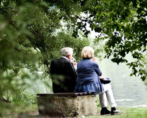 two people sitting on pavement facing on body of water