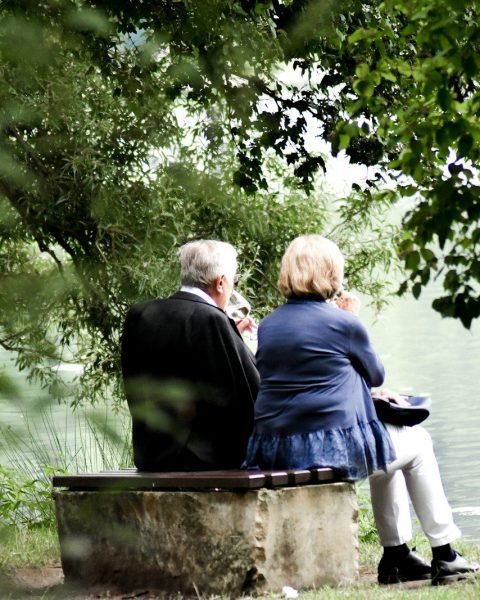 two people sitting on pavement facing on body of water