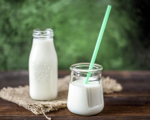 Een yoghurtdrankje met plantensterolen op een ontbijttafel naast een bord met boterhammen