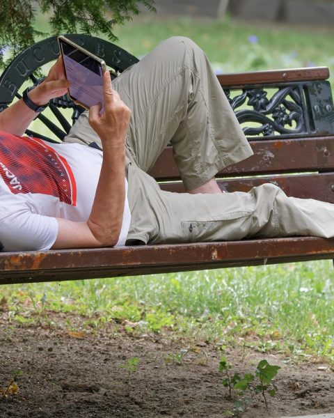 Senior die ontspannen buiten zit te lezen op een e-reader