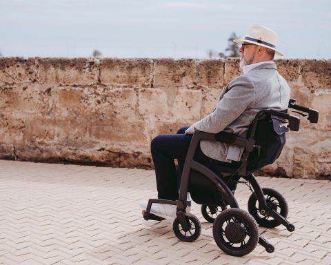 Oudere vrouw loopt binnenshuis met een rollator door een smalle gang