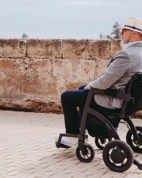 Oudere vrouw loopt binnenshuis met een rollator door een smalle gang