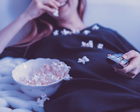 Een oudere vrouw zit comfortabel op de bank televisie te kijken