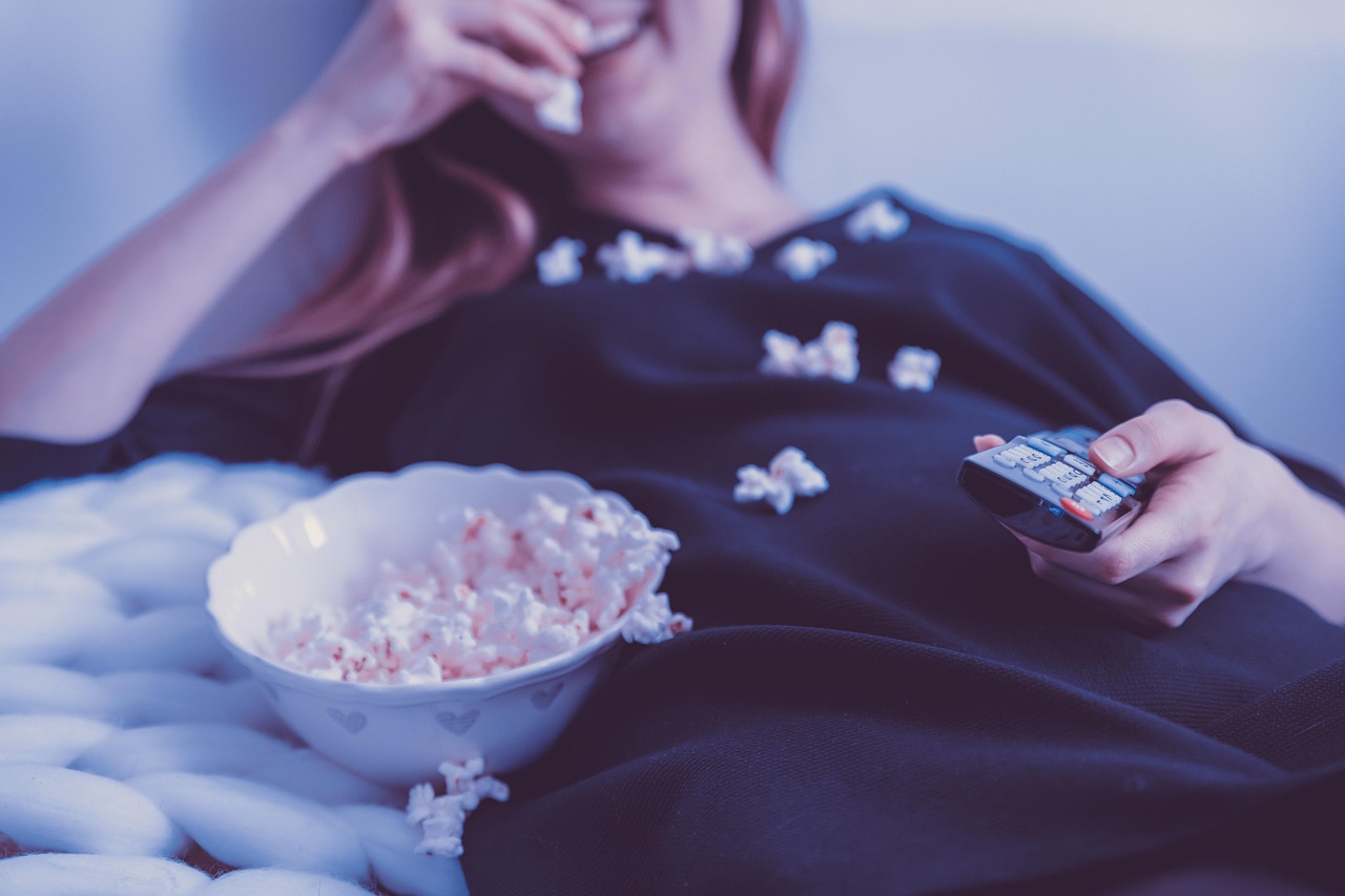 Een oudere vrouw zit comfortabel op de bank televisie te kijken