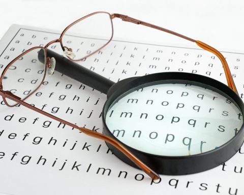 Oudere vrouw die met een vergrootglas een boek leest bij een raam