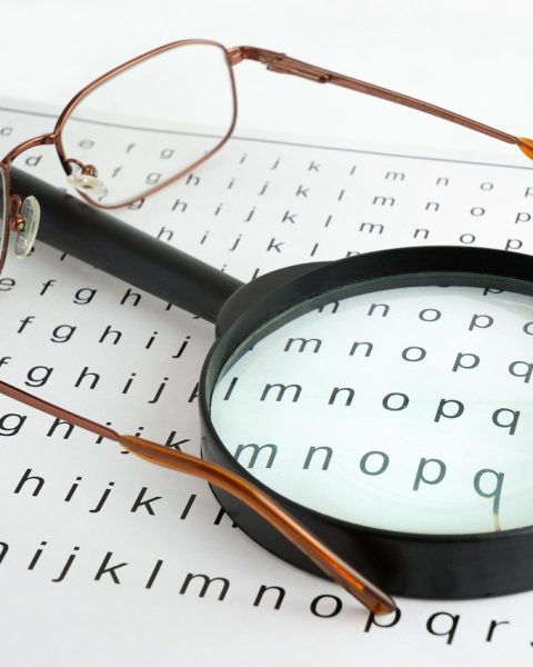 Oudere vrouw die met een vergrootglas een boek leest bij een raam