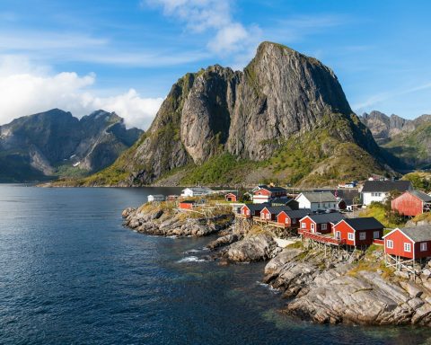 a group of houses by a body of water with mountains in the background with Lofoten in the background