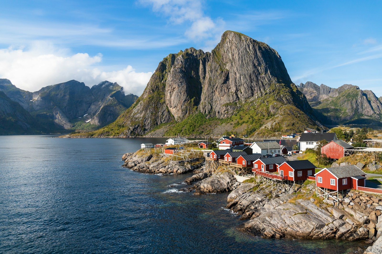 a group of houses by a body of water with mountains in the background with Lofoten in the background
