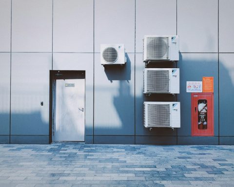 Four air conditioning units on a grey panelled wall beside a red fire cabinet