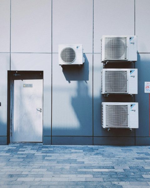 Four air conditioning units on a grey panelled wall beside a red fire cabinet