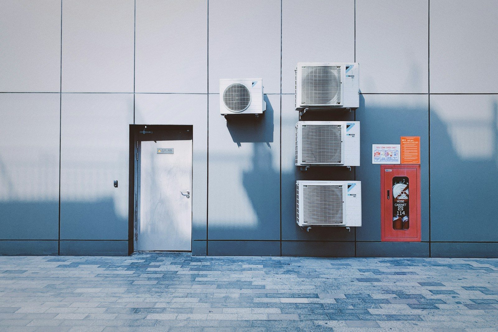 Four air conditioning units on a grey panelled wall beside a red fire cabinet