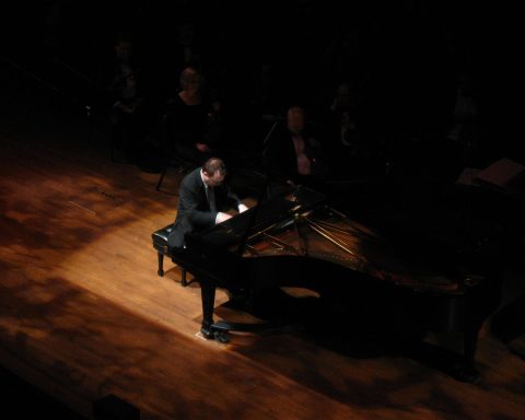 Een pianist speelt op een vleugel op een verlicht podium voor een publiek