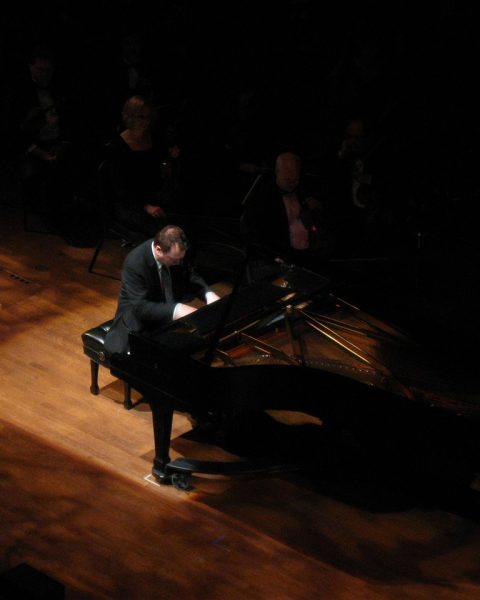 Een pianist speelt op een vleugel op een verlicht podium voor een publiek