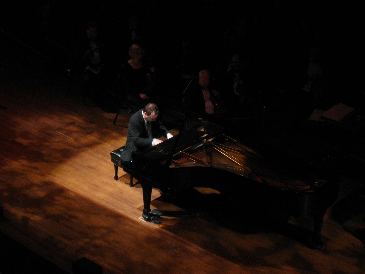 Een pianist speelt op een vleugel op een verlicht podium voor een publiek