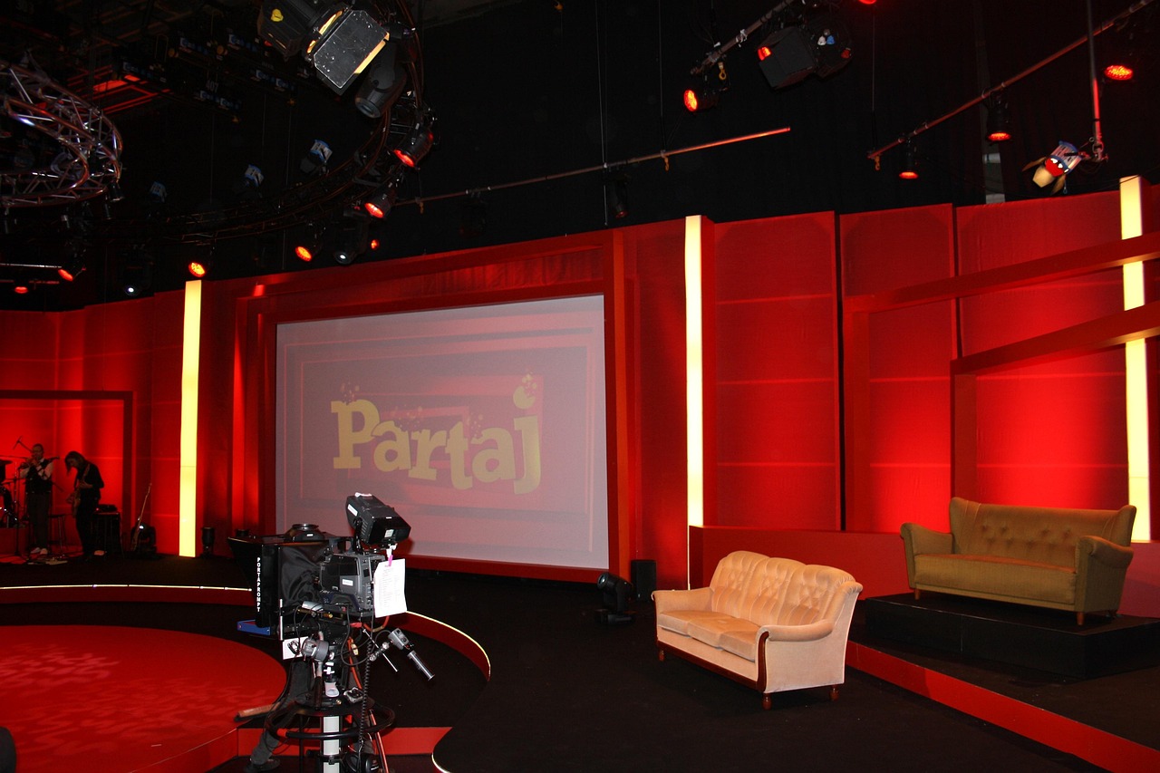 Een oudere man met een doorleefde uitstraling zit in een televisiestudio, klaar voor een interview